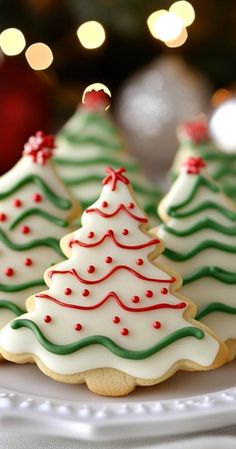 three decorated christmas cookies on a plate with lights in the backgroung behind them