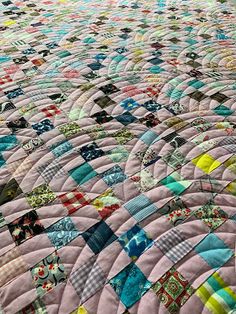 a large quilt is laying on top of a bed with many different colors and patterns