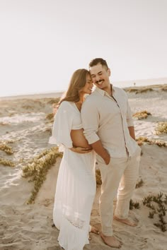 a man and woman standing on top of a sandy beach