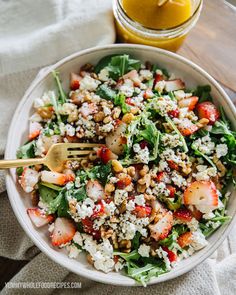 a salad with strawberries, nuts and feta cheese in a bowl next to a glass of orange juice