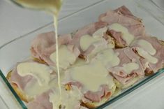 ham and cheese on bread being drizzled with white sauce in a glass dish