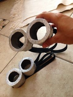 a person holding three silver objects on top of a tile floor next to a black cord