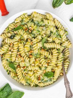 a white bowl filled with pasta and spinach on top of a table next to red peppers