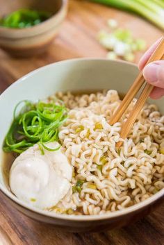 someone is holding chopsticks over a bowl of ramen with noodles and scallions