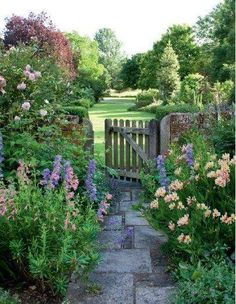 an image of a garden setting with flowers and plants in the foreground, along with a path leading to a gate