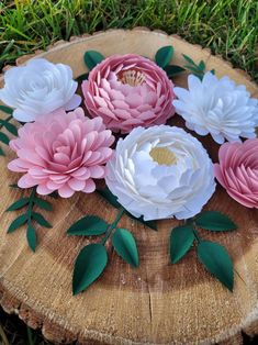 pink and white paper flowers sitting on top of a piece of wood in the grass