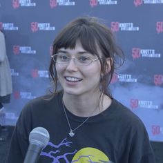 a woman with glasses and a microphone in front of a sign that says 50 minutes