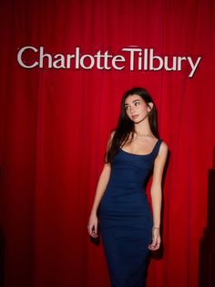 a woman in a blue dress standing next to a red curtain with the charlotte tilbury logo on it