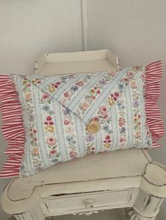 a pillow sitting on top of a white table next to a small chest with drawers