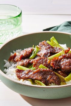 a bowl filled with rice and meat on top of a white table next to a glass of water