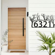 a house number sign next to a door with a plant in the foreground and a potted plant behind it