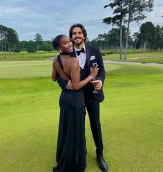 a man and woman in formal wear posing for a photo on the golf course with their arms around each other