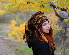 a woman with red hair wearing a crocheted hat and scarf under a tree