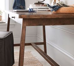 a wooden table topped with lots of books and a bag on top of it next to a window