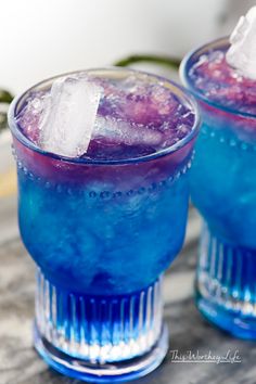 two glasses filled with blue liquid and ice sitting on top of a table next to each other