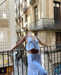 a woman is standing on a balcony with her arms spread out and looking at the street