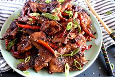 a white plate topped with meat and veggies next to two chopsticks