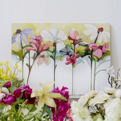 some flowers are sitting on a table next to a painting and vases with flowers in them