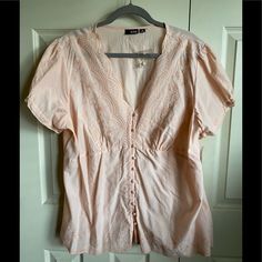 Peach, Short Sleeve, Button Up Blouse With Decorative Stitching On The Front At Shoulders, V Neck And Along The Bottom, Front And Back. The Sleeves Have A Bit Of Elastic Gathering At The Top And There’s A Slight Taper At The Top Of The Waist. It’s Never Been Worn. It Has All The Buttons Plus One Extra. Feminine Buttoned Tops For Beach, Feminine Buttoned Tops For The Beach, Peach Shorts, Decorative Stitching, Button Up Blouse, Short Sleeve Button Up, V Neck Blouse, Cream White, Button Up