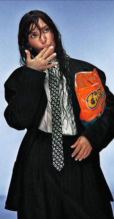 a man with long hair wearing a suit and tie holding an orange boxing glove over his mouth