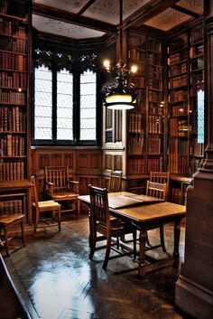 an old library with many bookshelves and wooden tables in the center, along with two tall stained glass windows