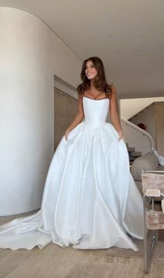 a woman in a white wedding dress standing next to a table and chair, smiling at the camera