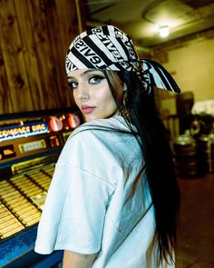 a woman standing in front of a row of pinball machines wearing a bandana