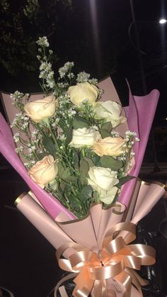 a bouquet of roses is wrapped in pink paper and tied with gold ribbon on a table