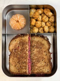 a sandwich with meat, potatoes and an orange in a metal lunch tray on a white countertop