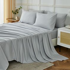 a bed covered in grey sheets and pillows