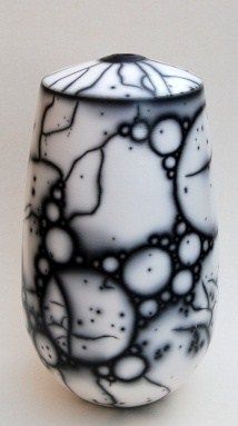 a black and white glass vase sitting on top of a table next to a wall