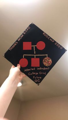 a person holding up a black and red graduation cap