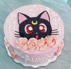 a pink cake with a black cat face on it's side and roses around the edges