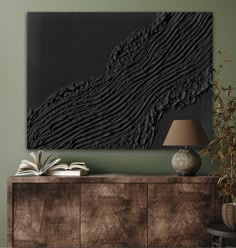 a large black piece of art hanging on the wall next to a table with a lamp