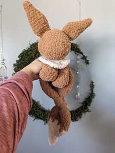 a person holding up a stuffed animal in front of a wreath with ornaments hanging from it