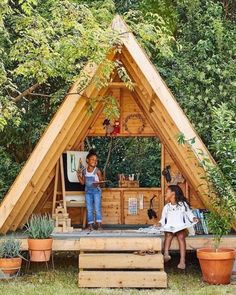 two people are sitting in front of a small wooden structure that is made out of wood