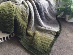 a green and white crocheted blanket sitting on the floor next to a potted plant