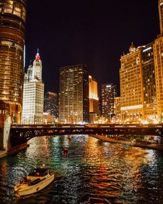 a boat floating on top of a river next to tall buildings in the city at night