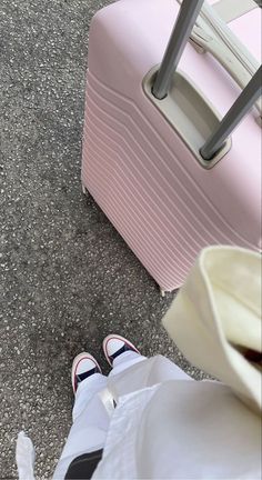 a person standing next to a pink piece of luggage on the ground with their feet up