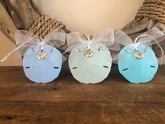 three small blue and green sand dollar ornaments on a wooden table next to driftwood