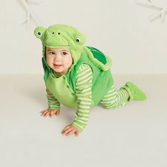 a baby in a frog costume crawling on the floor with one leg up and two hands behind his head