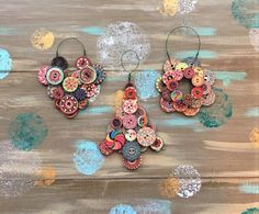 two pairs of earrings made out of buttons on top of a wooden table with paint splatters in the background