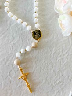 Engage with the elegant beauty of our Lily Rosary - Mary's Humility in stunning white. Delicate and prayerful, this modern Rosary embodies Mary's purity. Let your prayers be lifted to Mary as you wander through the garden of her virtue, perfect for those seeking a sophisticated touch to their spiritual practice. The centerpiece features an image of Our Lady crowned with flowers and "Ave Maria" inscribed on the back. Approx 15" 8mm glass beads in whites, with cream Our Father beads Ethically made Adjustable White Rosary As Gift, Elegant White Rosary For First Communion, Adjustable White Rosary For First Communion, Elegant Pearl White Pearl Rosary, Spiritual Pearl White Rosary Gift, White Pearl Spiritual Rosary, Catholic Candles, White Cross-shaped Rosary For Baptism, Hand-strung Rosary With Round Beads As Gift