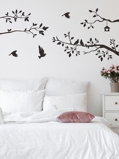 a white bed sitting next to a wall with birds on it's tree branches