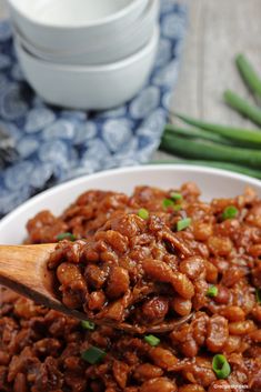 a white bowl filled with cooked beans and green onions on top of a wooden spoon