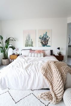 a bed with white sheets and blankets on top of it in a room filled with plants