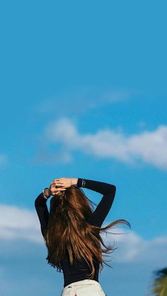 a woman with long hair standing in front of palm trees and looking up at the sky