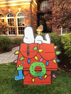 a large cardboard christmas decoration in front of a house with snoopy on it's roof