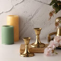 three gold candlesticks sitting on top of a white counter next to flowers and vase