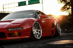 a red sports car parked in front of an overpass with the sun behind it